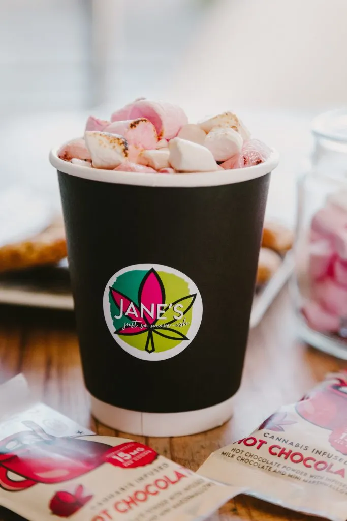 Jane's Edibles branded hot chocolate topped with marshmallows beside cannabis infused hot chocolate sachets